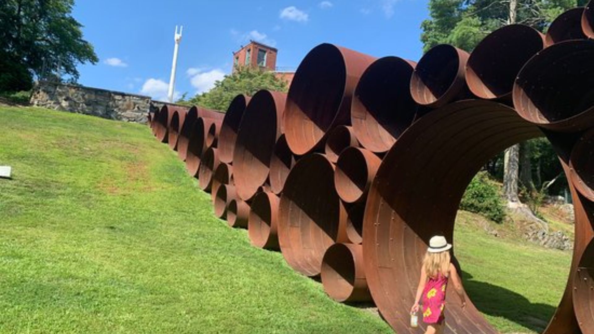 Child in costume near a large outdoor sculpture, fall foliage in background